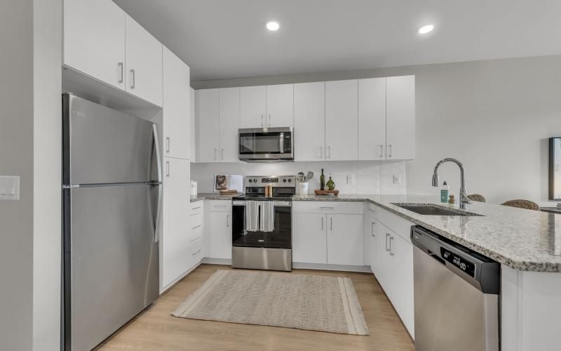 An interior view of a kitchen with white cabinets and stainless steel appliances, including a fridge, microwave, oven, and a dishwasher at Darby at Briarcliff brand new apartments in Kansas City, MO.
